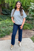 Woman wearing Grey Floral & Pearl Detail Short Sleeve Sweater by Entro and blue jeans while outside with greenery around. 