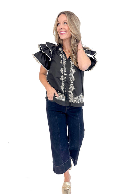 Front view of woman wearing Black Center Embroidered Ruffle Sleeve Top by Entro and blue jeans. 