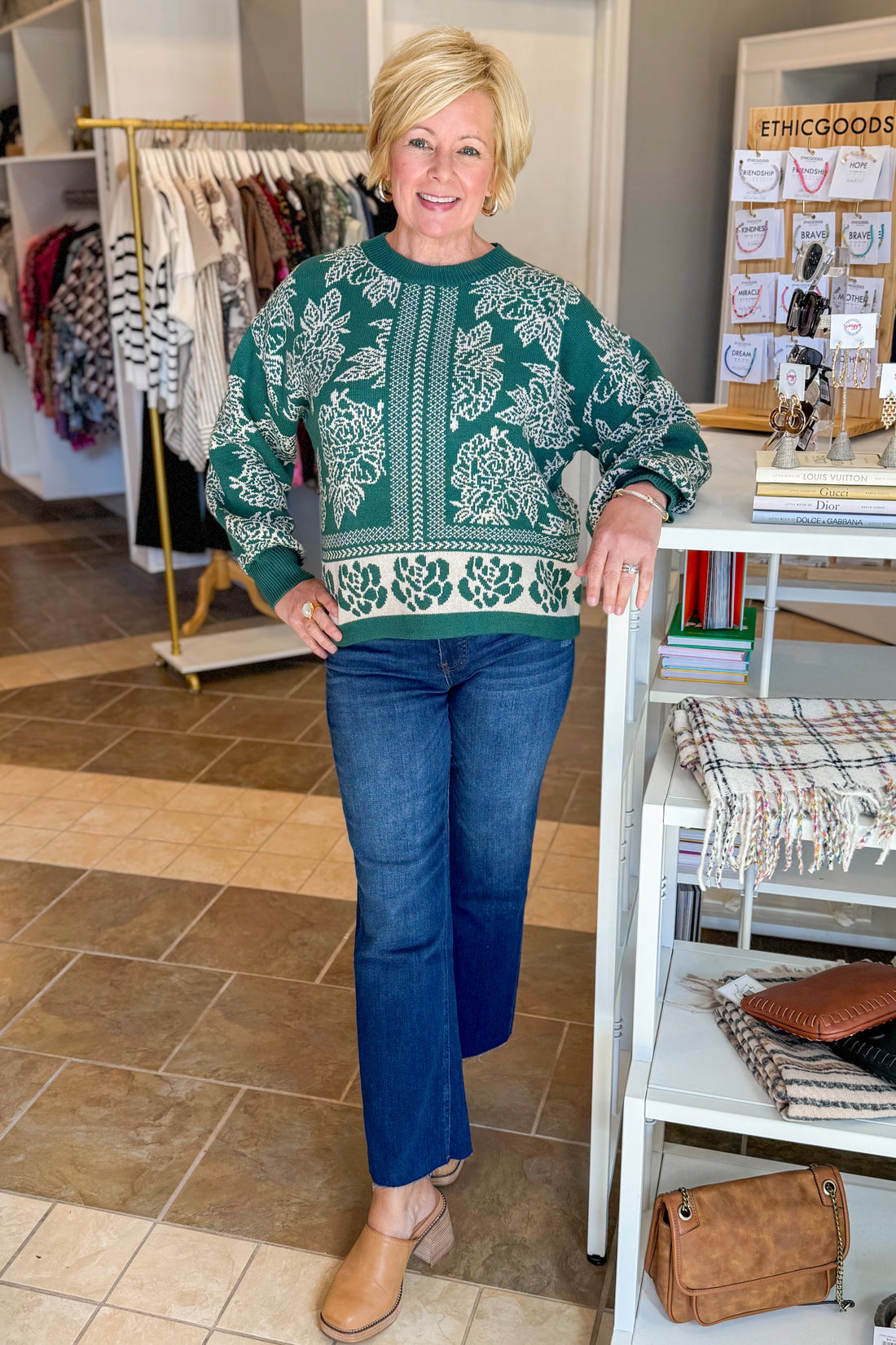 Woman wearing a green patterned sweater and blue jeans standing in a store.