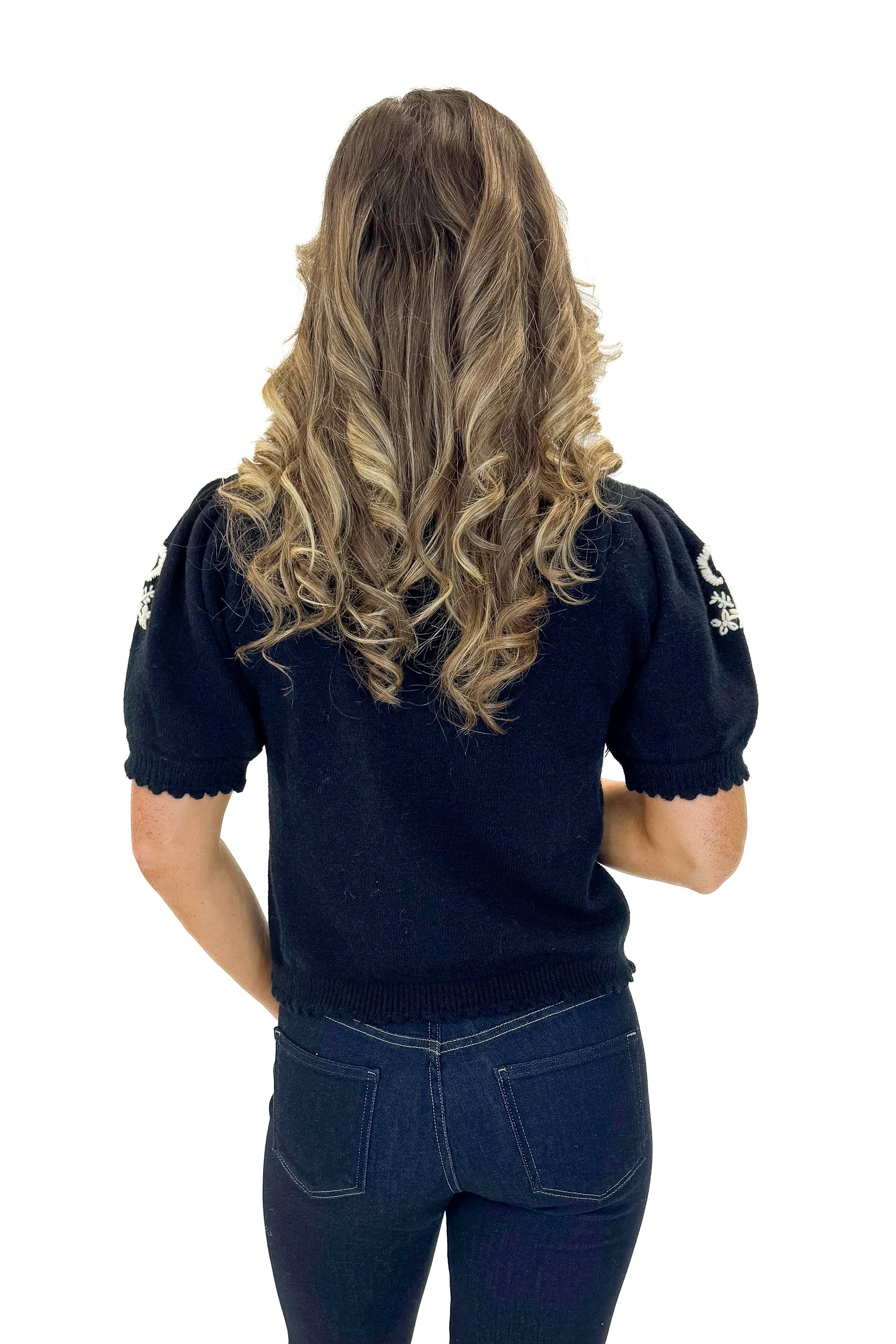 Back view of woman wearing Black Center Embroidered Short Sleeve Cardigan with jeans against white studio background.