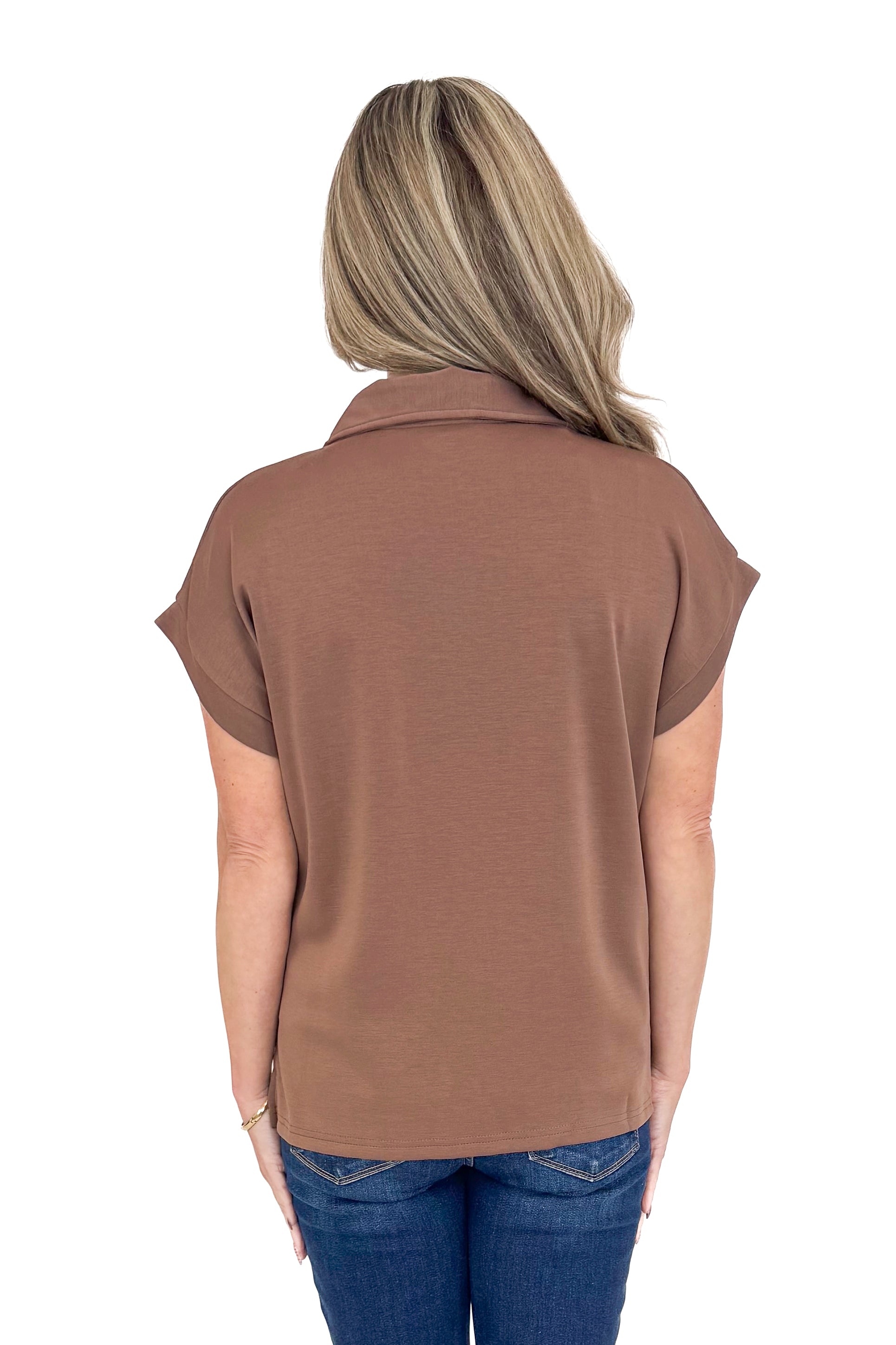 Back view of woman wearing coffee color top with jeans against white studio background.