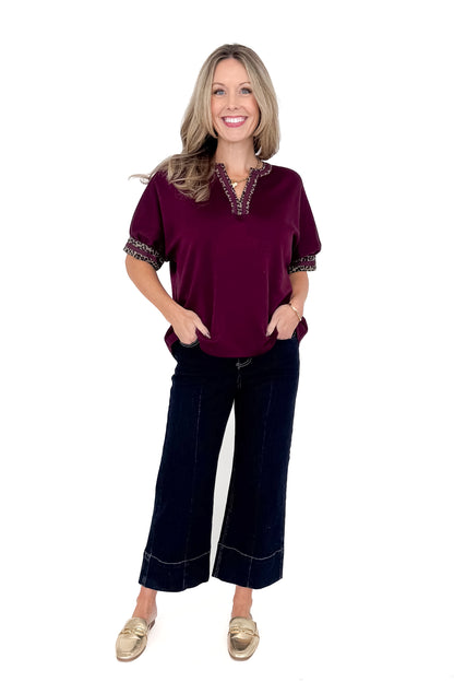 Front view of woman wearing burgundy top with jeans against white studio background.