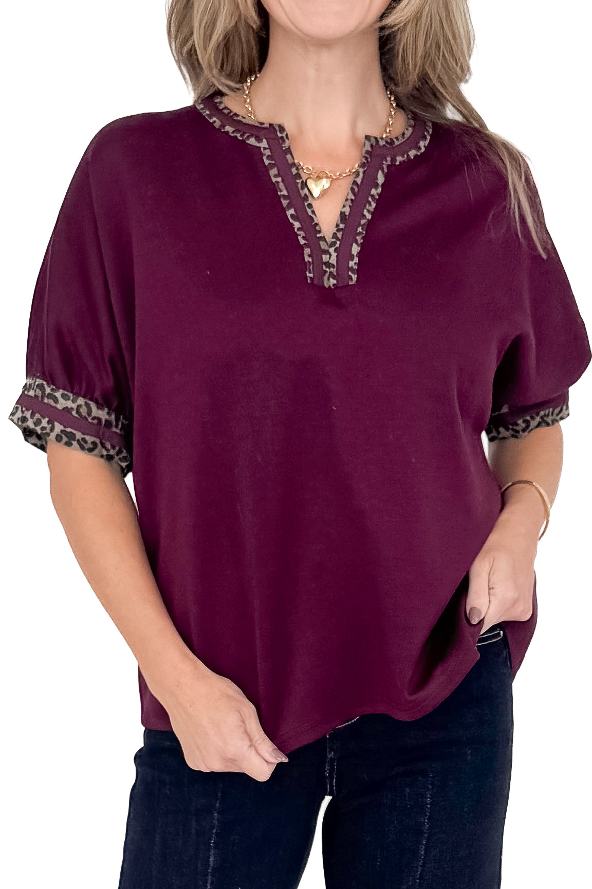 Front detail view of woman wearing burgundy top with jeans against white studio background.
