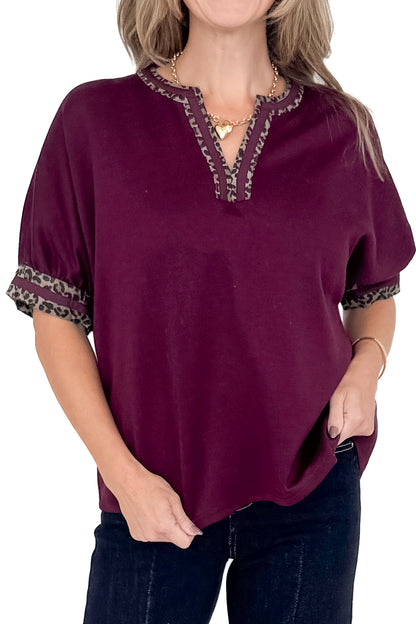 Front detail view of woman wearing burgundy top with jeans against white studio background.