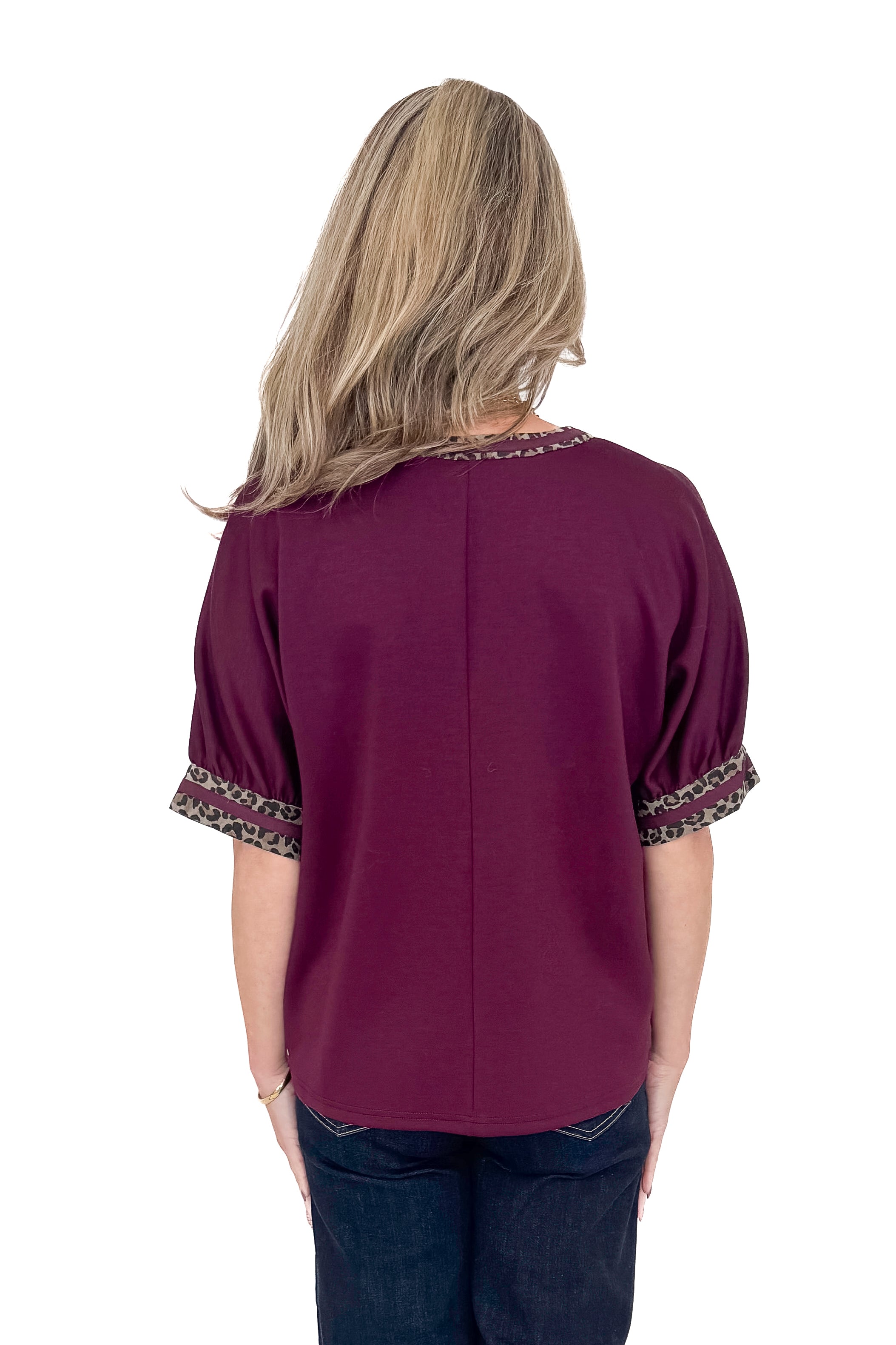 Back view of woman wearing burgundy top with jeans against white studio background.