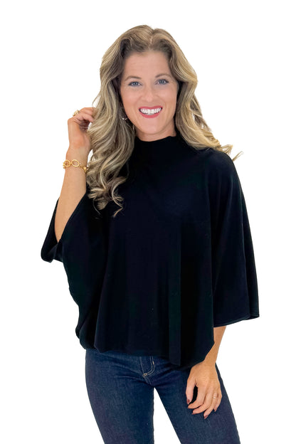 Front view of woman wearing Black Mock Neck Poncho Sweater with jeans against white studio background.