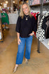 Front view of woman wearing Black Mock Neck Poncho Sweater with jeans at a boutique.