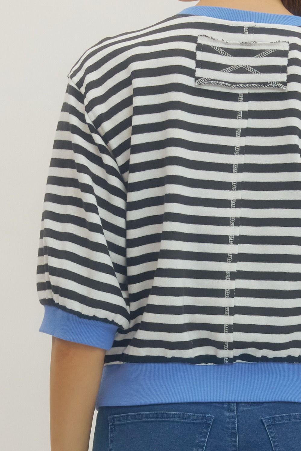 Back detail view of woman wearing Black Striped With Blue Lining 3/4 Sleeve Sweatshirt by Entro with jeans against a white background.