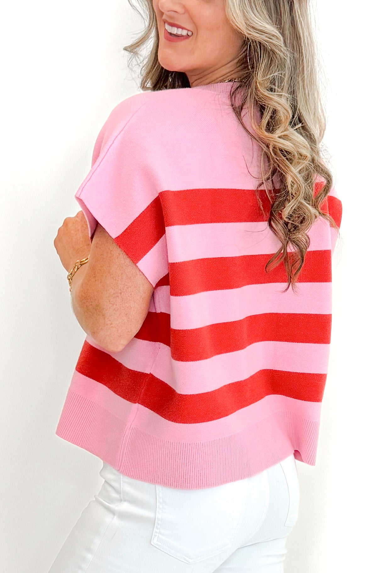 Side detail view of woman wearing Pink &amp; Red Sleeveless Sweater by Entro with jeans against white studio background.