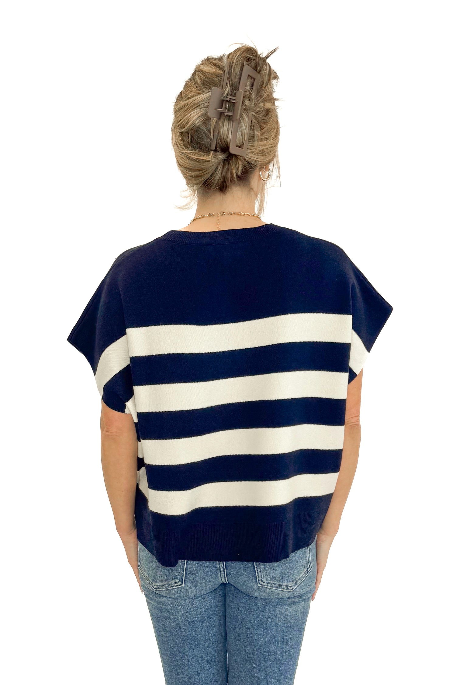 Back view of woman wearing Navy &amp; Cream Sleeveless Sweater by Entro with jeans against white studio background.