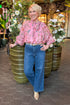 Front view of woman wearing Pink Floral Tie Neck Top by Entro with jeans at a restaurant.