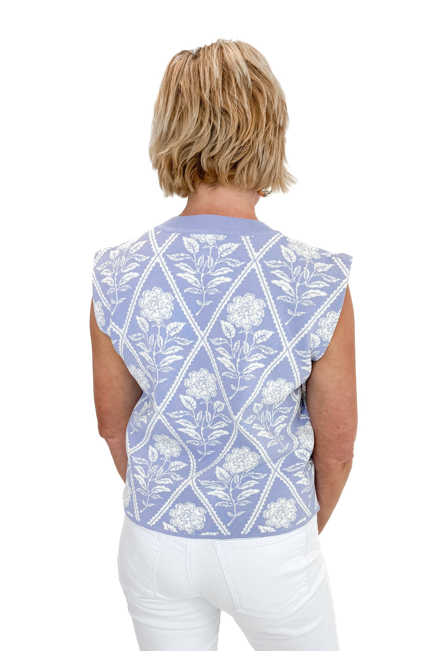 Back view of woman wearing Periwinkle Floral Printed Sleeveless Sweater by Entro with white jeans against white studio background.