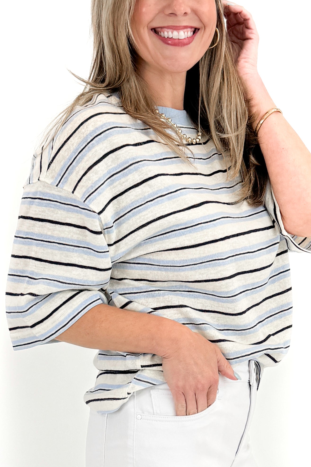 Side detail view of woman wearing Light Blue &amp; Navy Striped Top by Entro with jeans against white studio background.