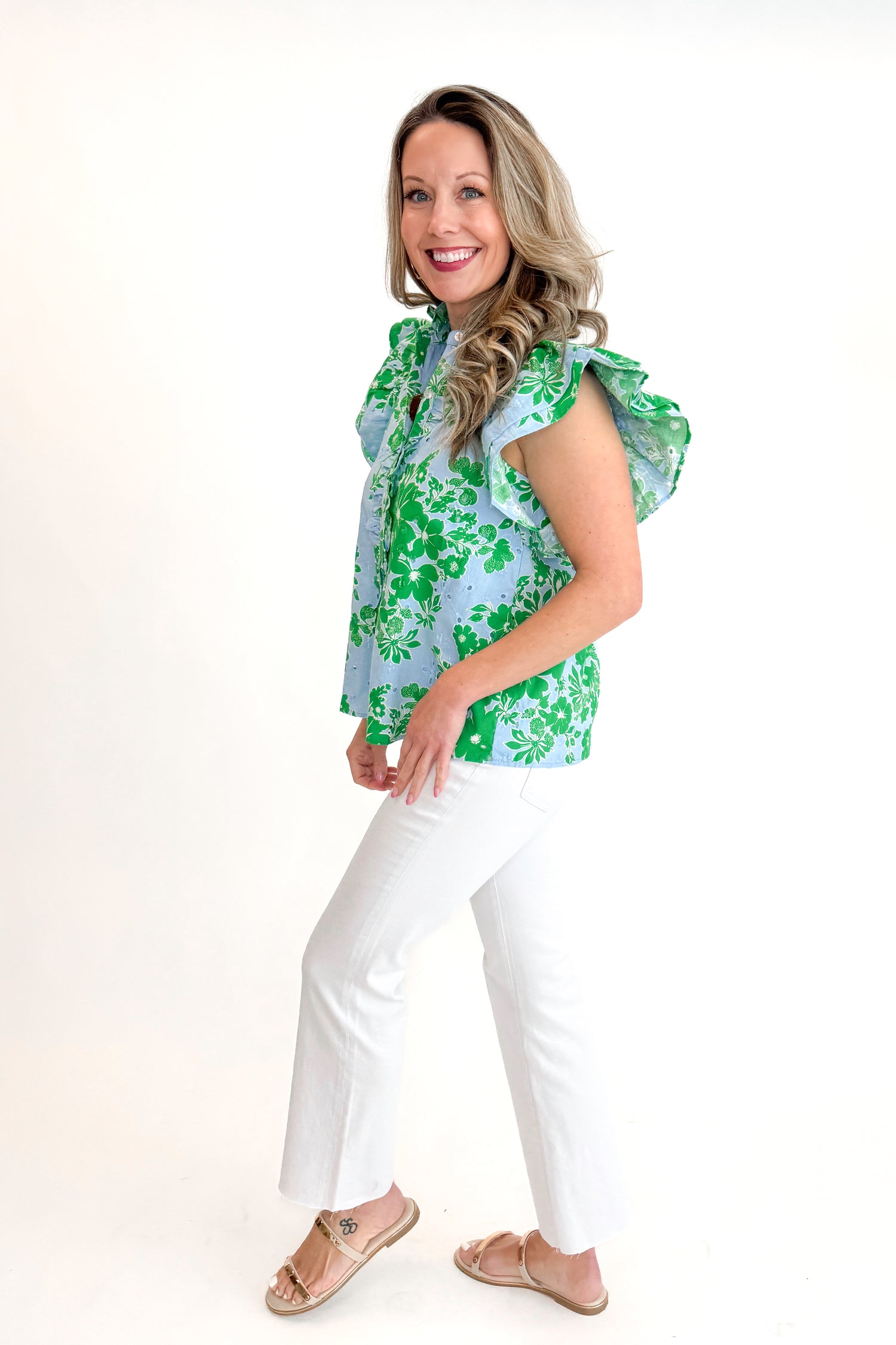 Side view of woman wearing Green &amp; Blue Floral Eyelet Top by Entro with white jeans against white studio background.