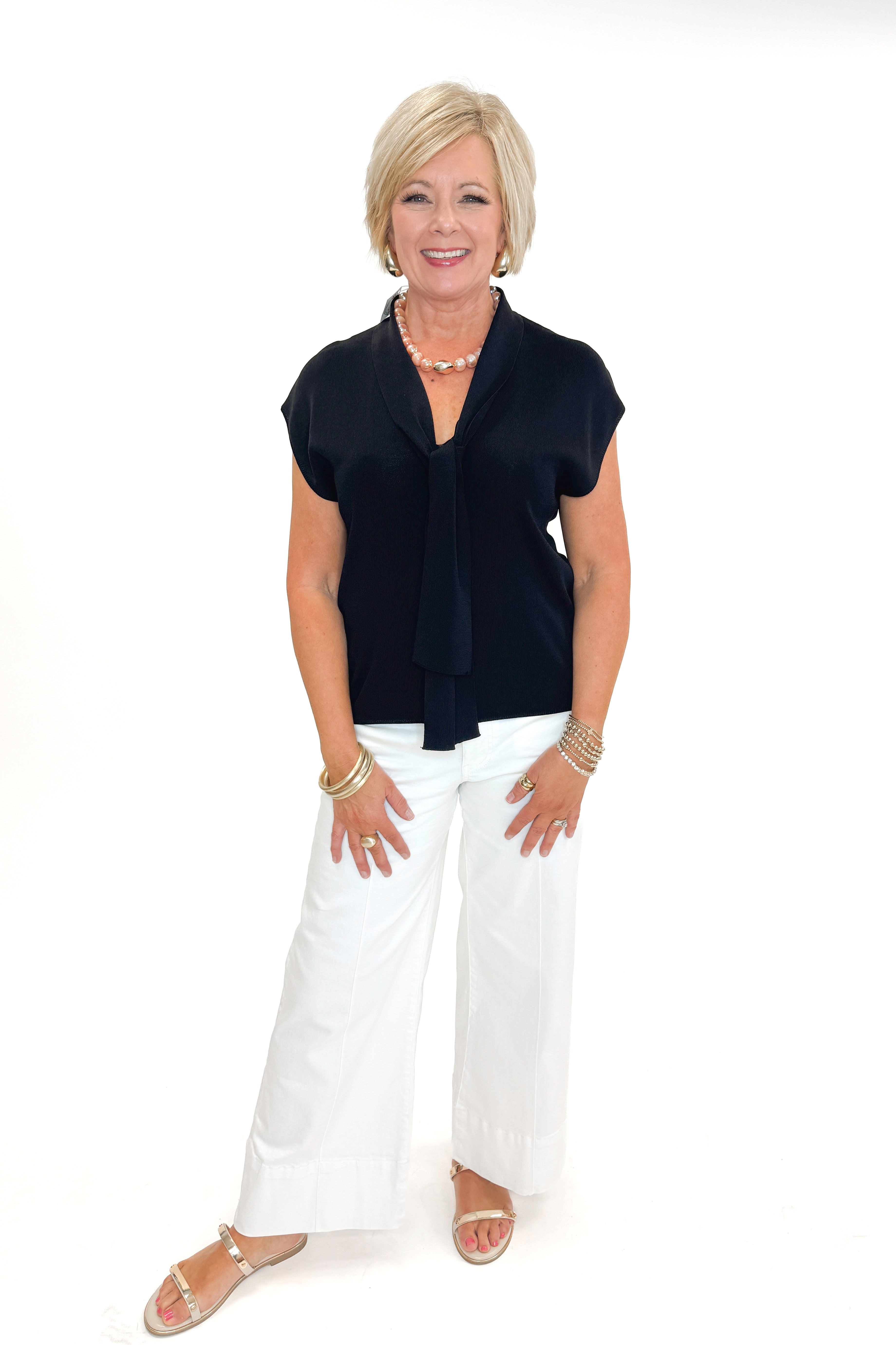 Front view of woman wearing Black Faux Layered Sweater Tank by Entro with jeans against white studio background.