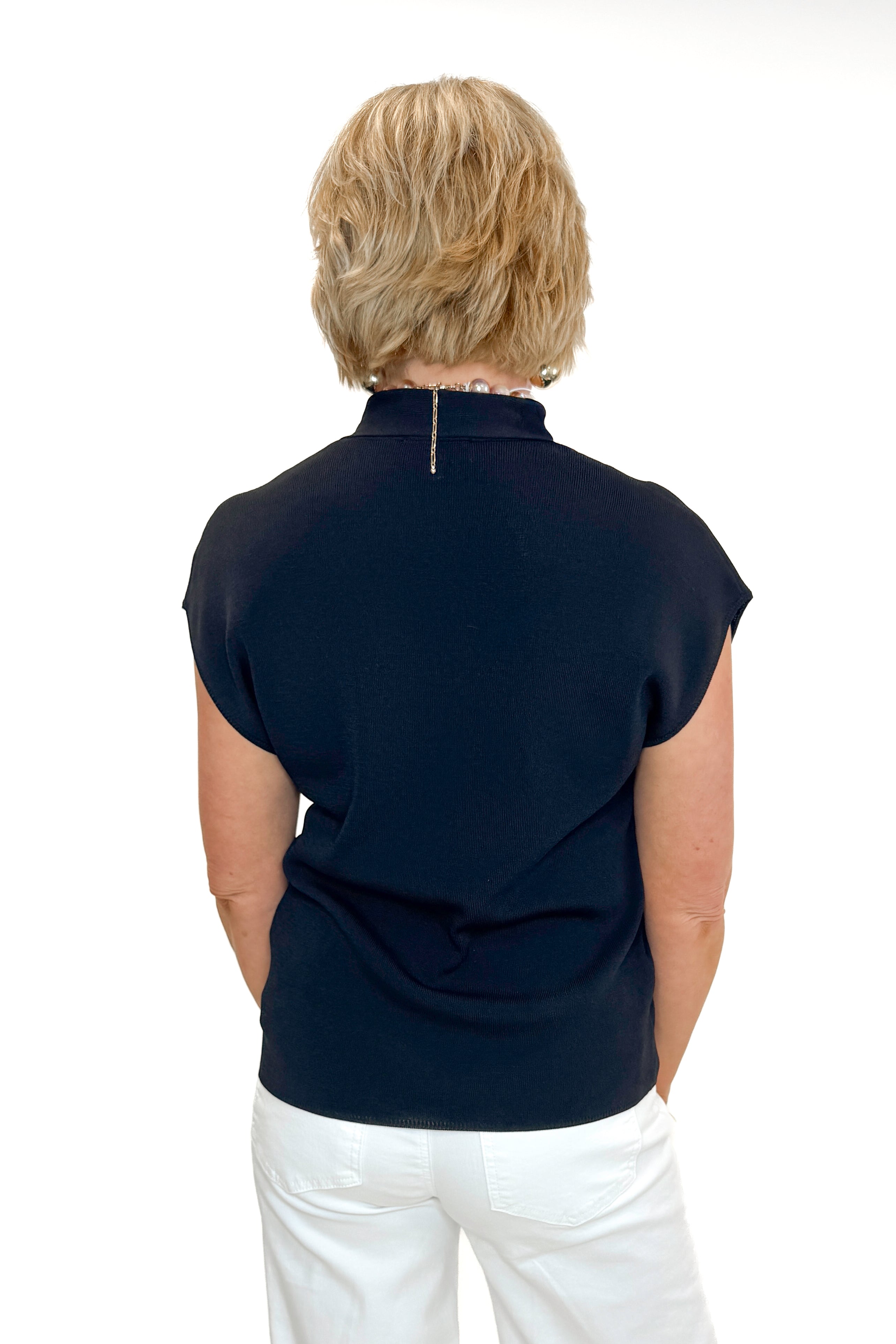 Back view of woman wearing Black Faux Layered Sweater Tank by Entro with jeans against white studio background.
