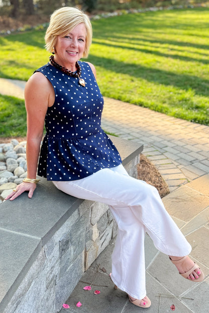 Front view of woman wearing Navy Polka Dot Peplum Tank by Entro with jeans at a garden.
