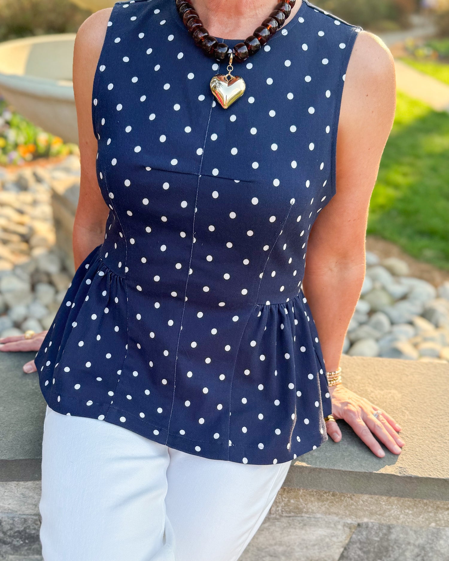 Front detail view of woman wearing Navy Polka Dot Peplum Tank by Entro with jeans at a garden.