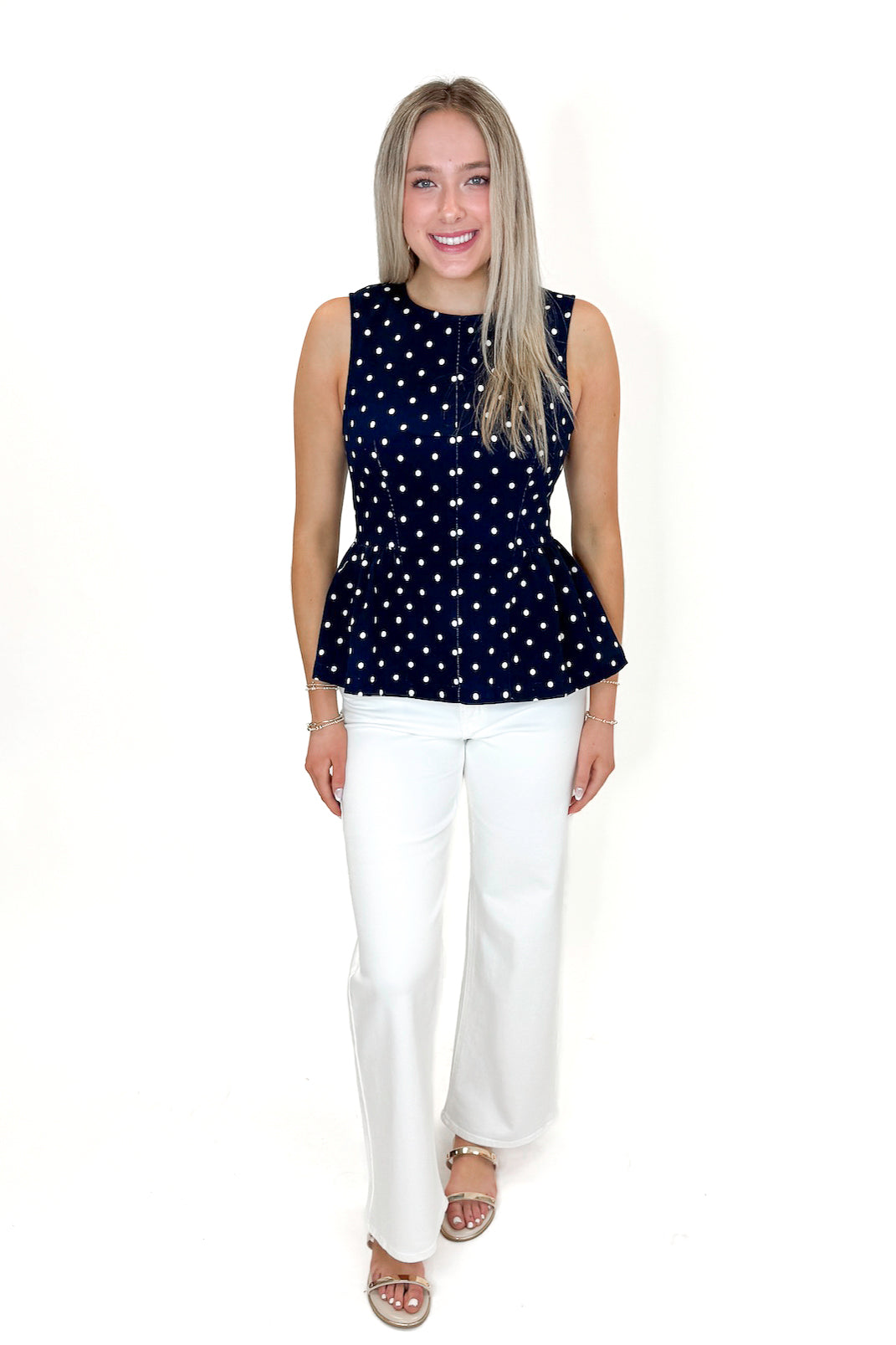 Front view of woman wearing Navy Polka Dot Peplum Tank by Entro with jeans against white studio background.