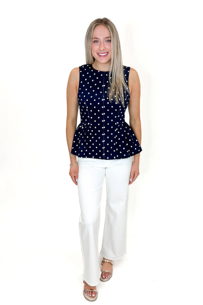 Front view of woman wearing Navy Polka Dot Peplum Tank by Entro with jeans against white studio background.