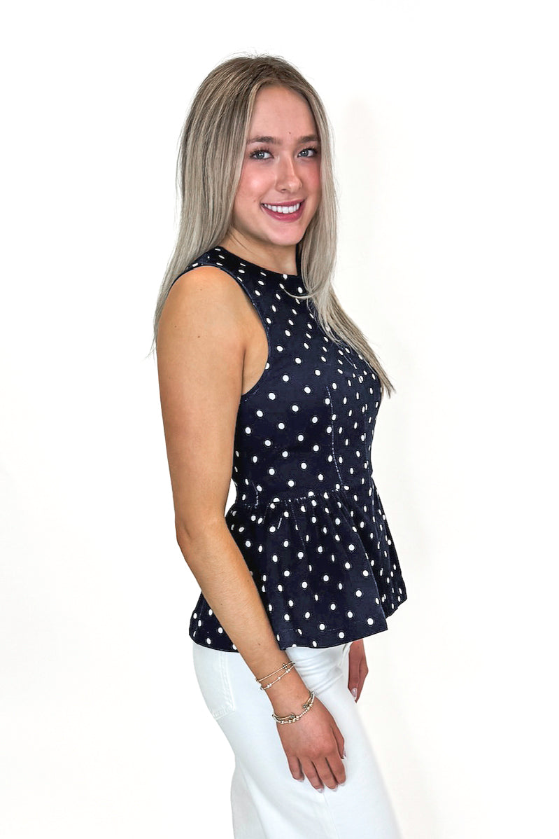 Side view of woman wearing Navy Polka Dot Peplum Tank by Entro with jeans against white studio background.