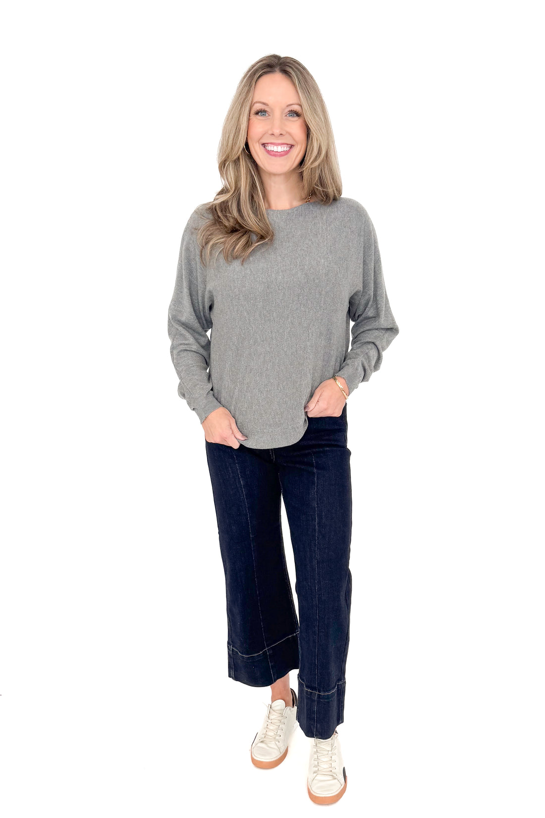 Front view of woman wearing grey sweater with jeans against white studio background.