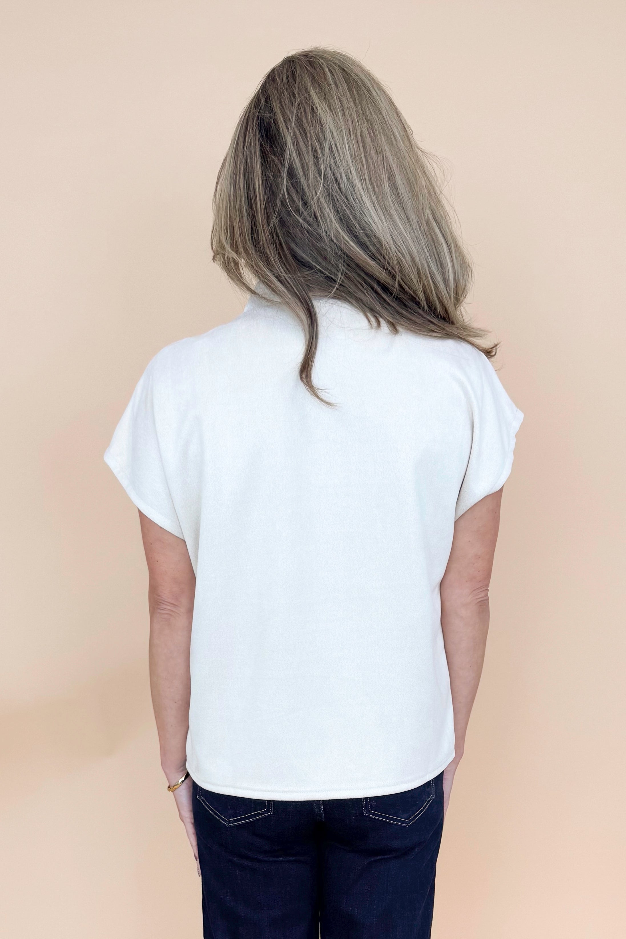 Back view of woman wearing Cream Suede Top by THML and jeans with tan background.
