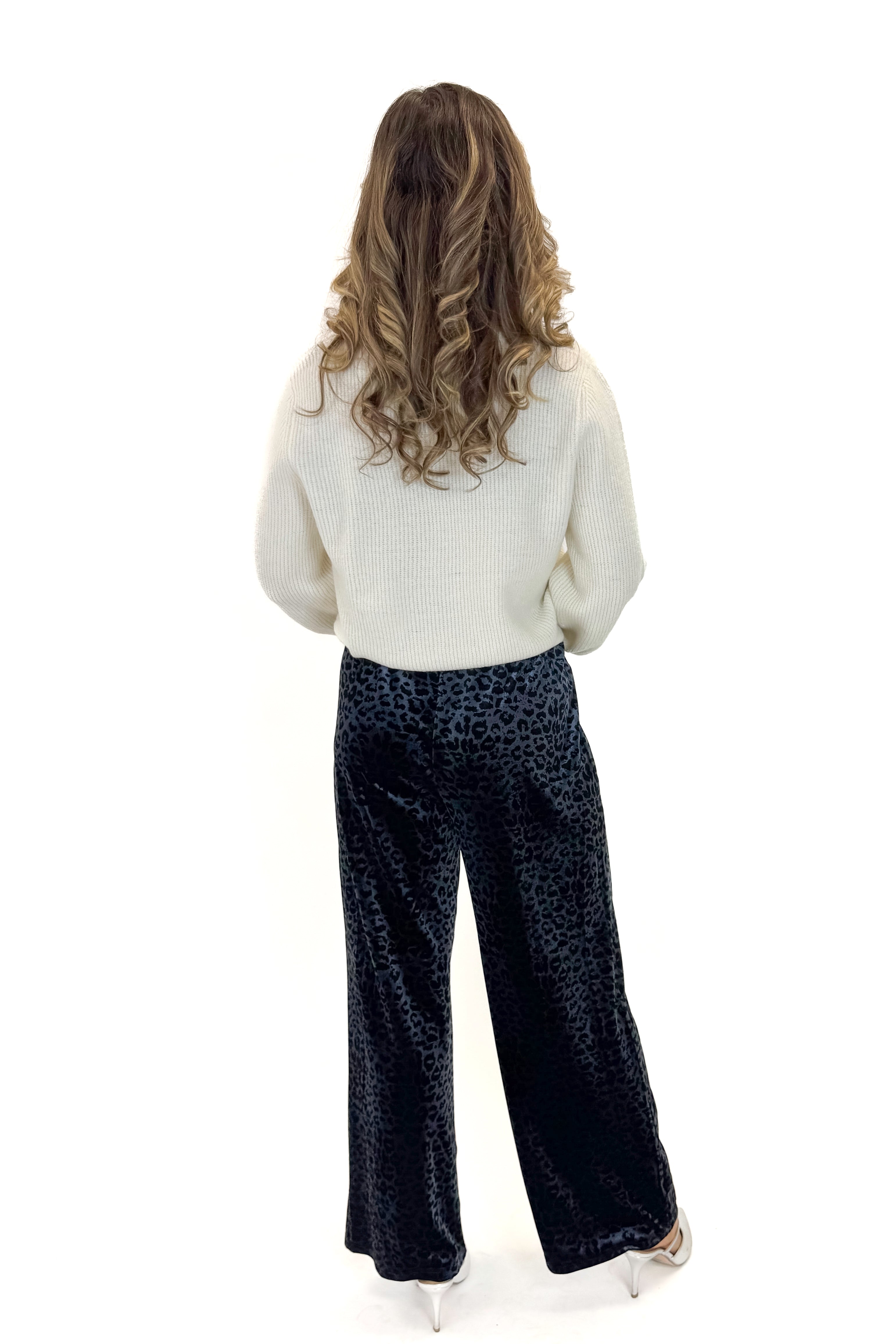 Back view of woman wearing Navy Velvet Leopard Print Pants with sweater against white studio background.