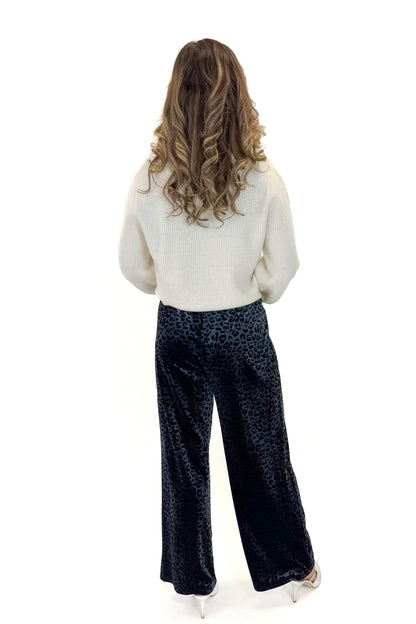 Back view of woman wearing Navy Velvet Leopard Print Pants with sweater against white studio background.