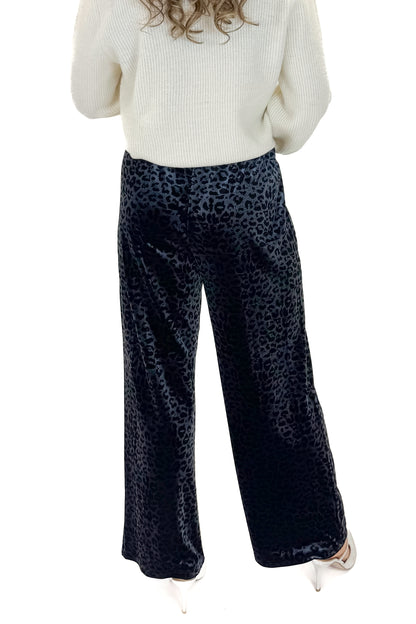 Back view of woman wearing Navy Velvet Leopard Print Pants with sweater against white studio background.