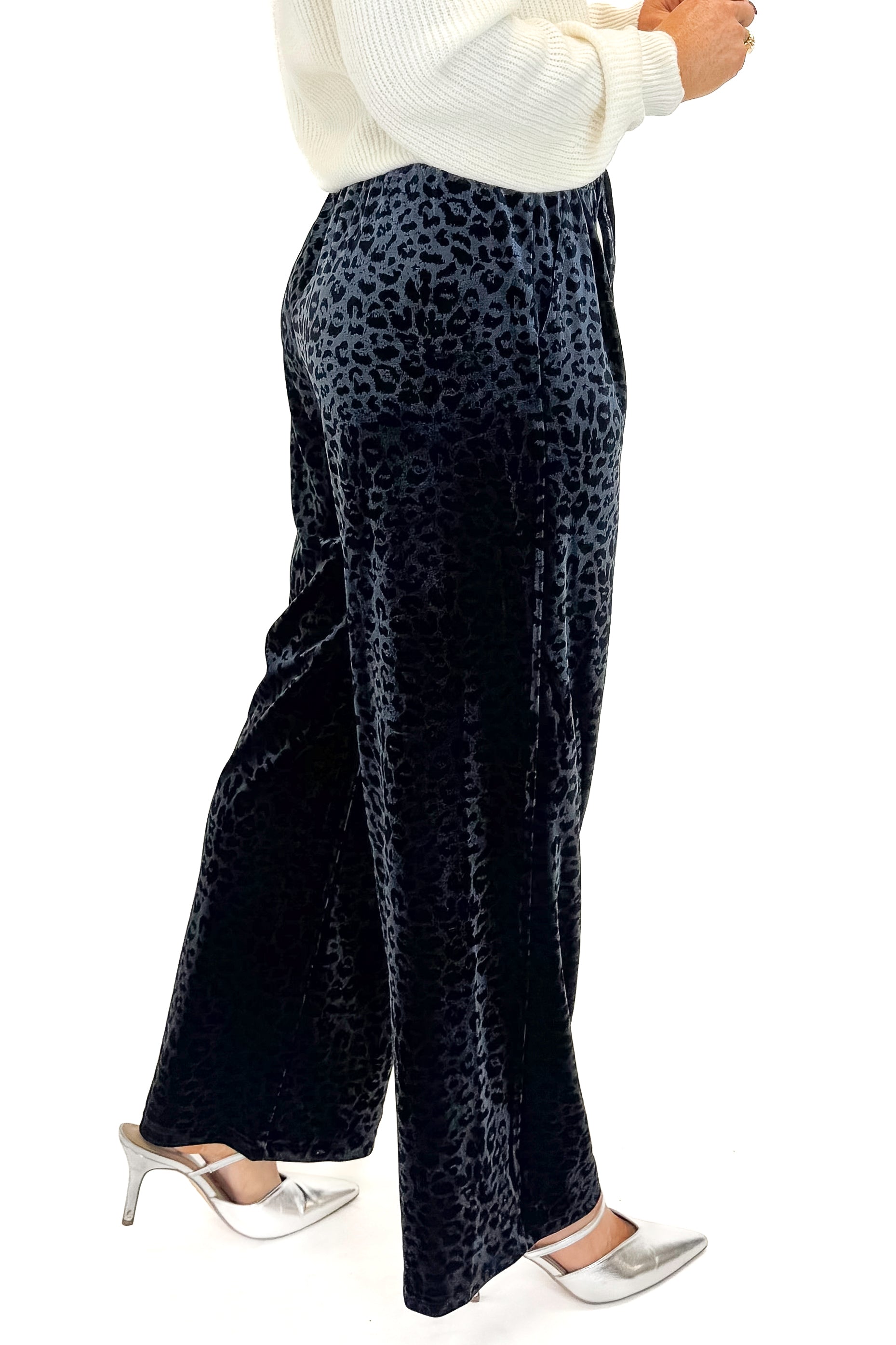 Side view of woman wearing Navy Velvet Leopard Print Pants with sweater against white studio background.