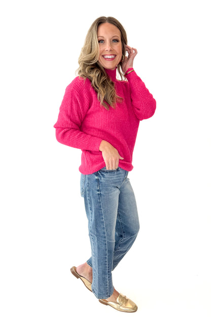 Side view of woman wearing Hot Pink Ribbed Turtleneck Sweater with jeans against white studio background.