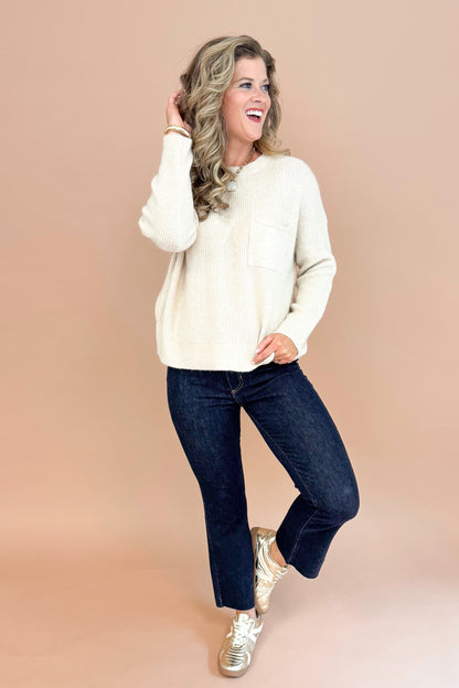 Woman wearing oatmeal colored crew neck pullover sweater with chest pocket detail and long sleeve full outfit.
