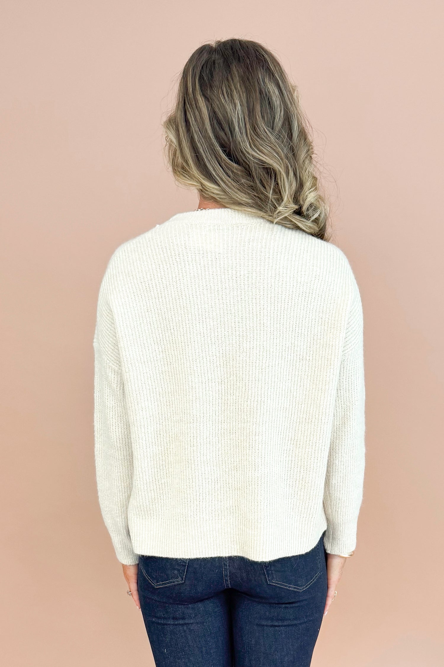 Woman wearing oatmeal colored crew neck pullover sweater long sleeve back view.