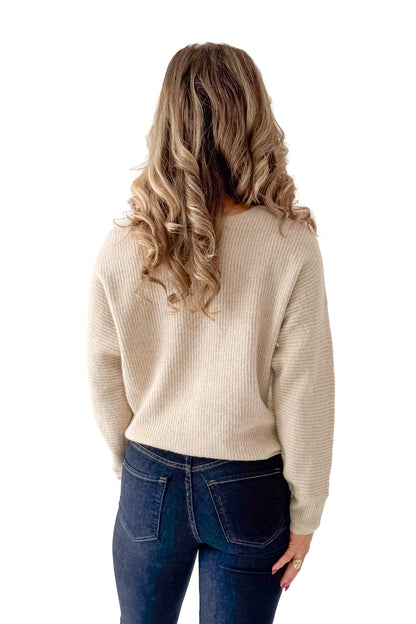 Back view of woman wearing Almond V-neck Sweater with jeans against white studio background.