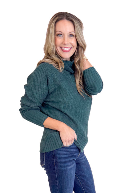 Woman wearing a dark green sweater and blue jeans on a white background