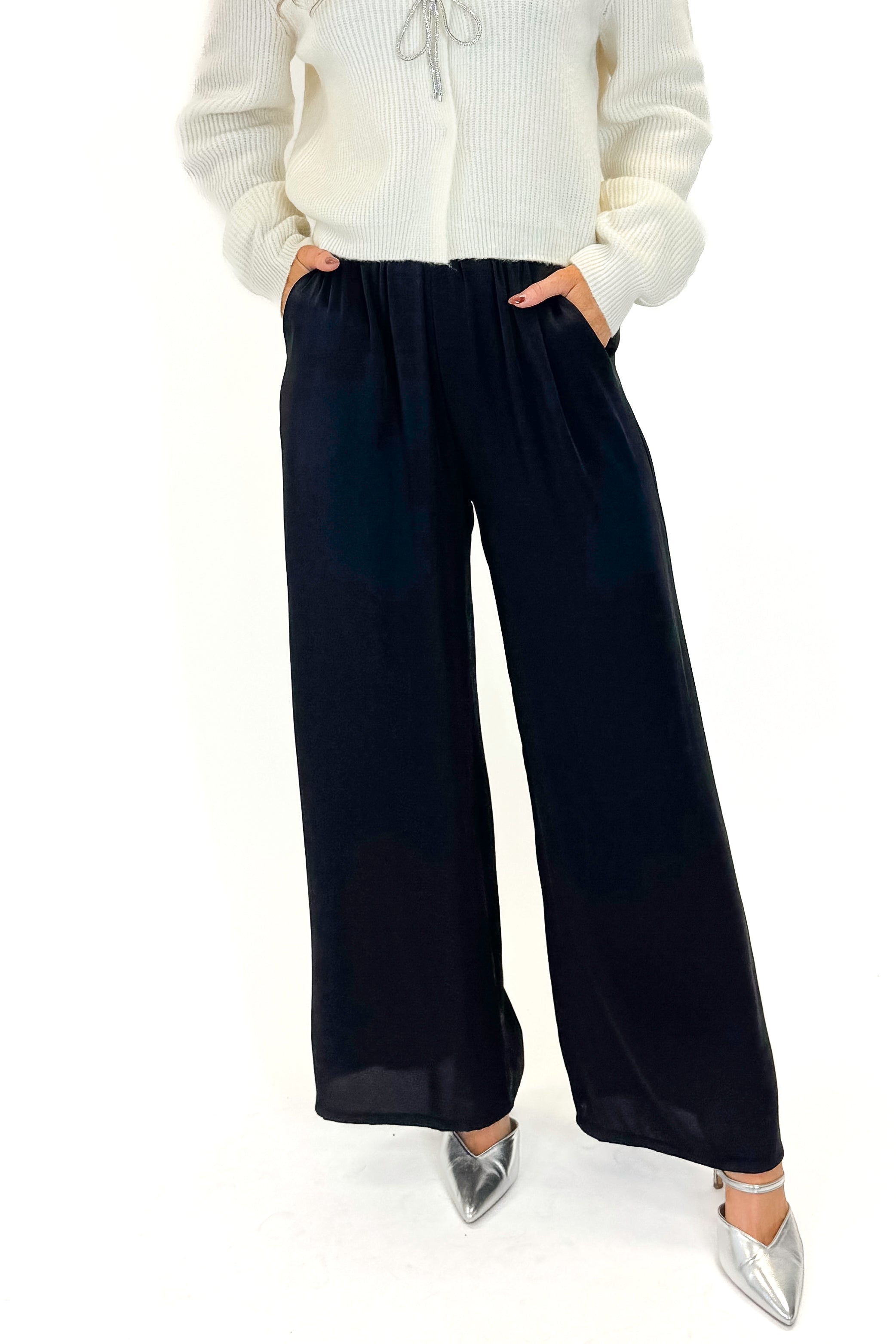Front detail view of woman wearing sweater with Black Satin Pants against white studio background.