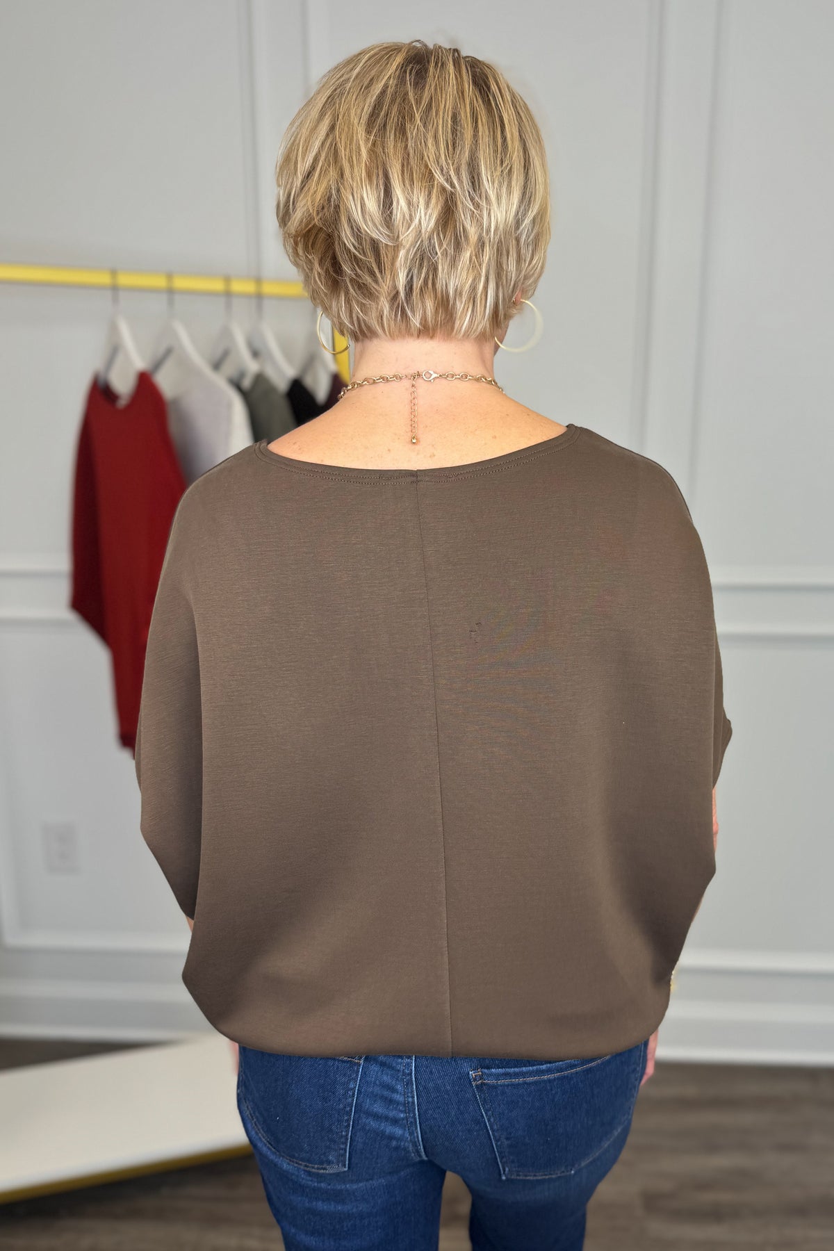 A woman viewed from behind wearing a brown long-sleeve top and blue jeans in a boutique setting.