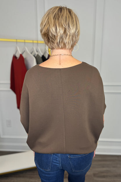 A woman viewed from behind wearing a brown long-sleeve top and blue jeans in a boutique setting.