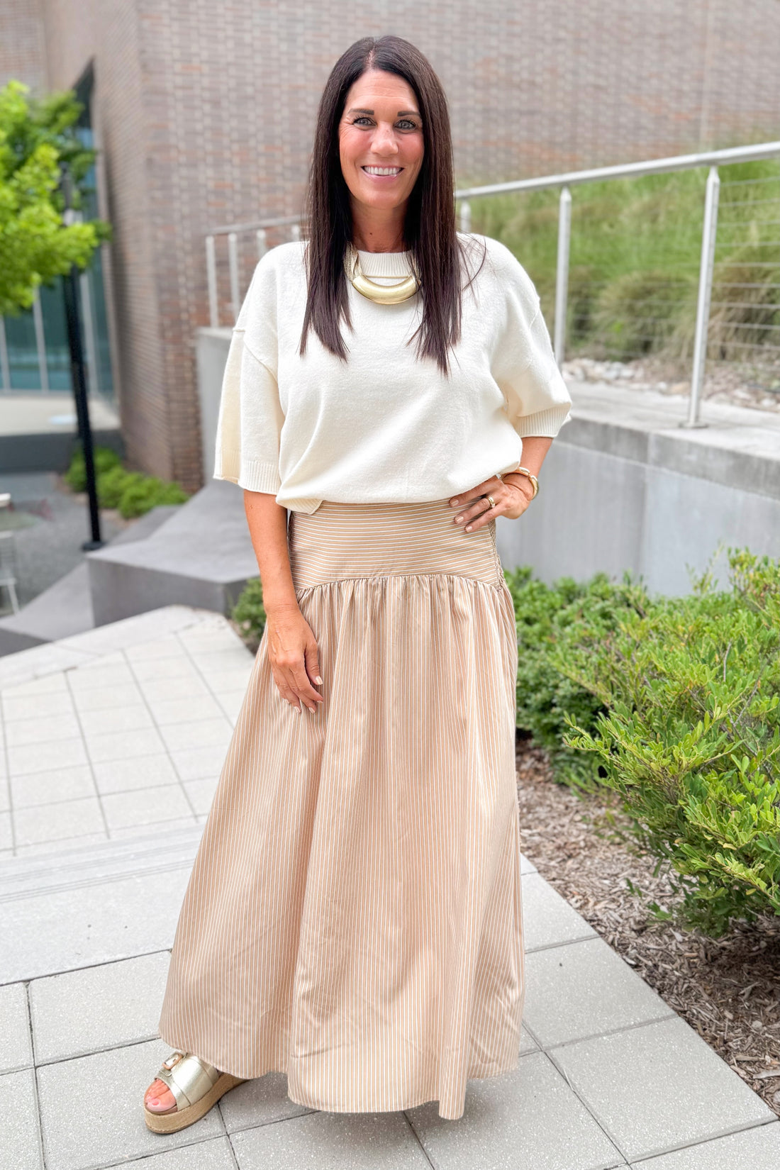 Front view of woman wearing Swagger Boutique’s Tan Striped Maxi Skirt with Cream 3/4 Sleeve Lightweight Sweater by Entro against white studio background.