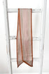 A long scarf with a tan base, brown borders, and beige geometric dot patterns, draped over a rustic white wooden ladder.