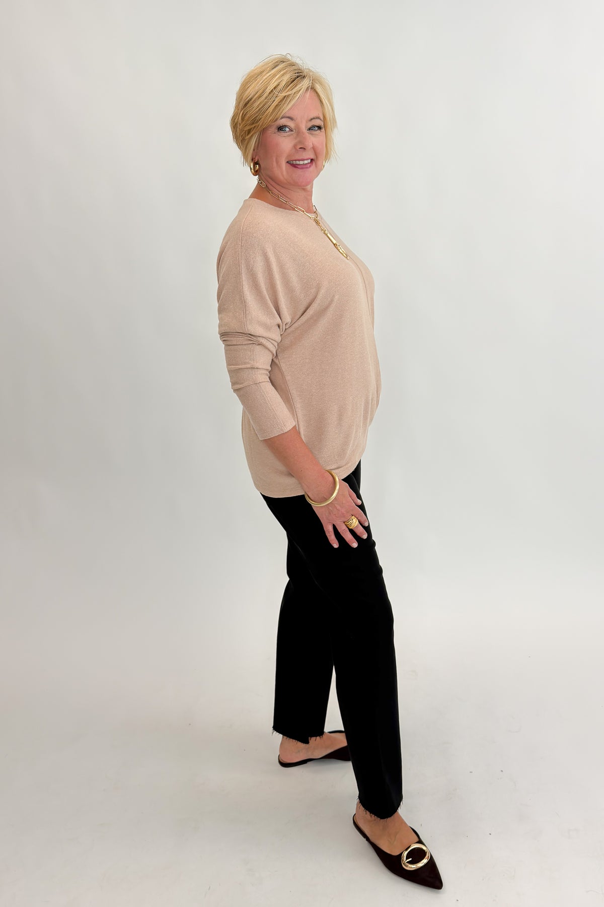 Side view of woman wearing Swagger Boutique’s Taupe Brushed Center Seam Top with jeans against white studio background.
