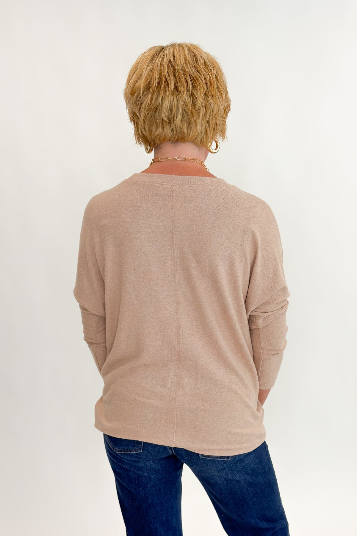 Back view of woman wearing Swagger Boutique’s Taupe Brushed Center Seam Top with jeans against white studio background.
