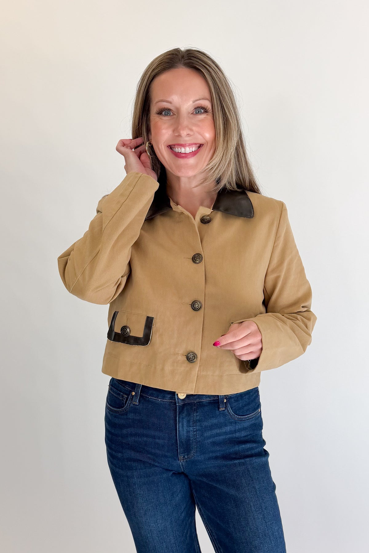 Front view of woman wearing Swagger Boutique’s Taupe Button Up Leather Collared Jacket with jeans against white studio background.