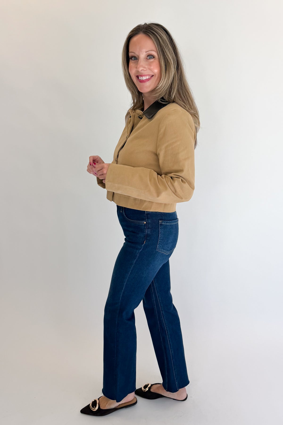 Side view of woman wearing Swagger Boutique’s Taupe Button Up Leather Collared Jacket with jeans against white studio background.