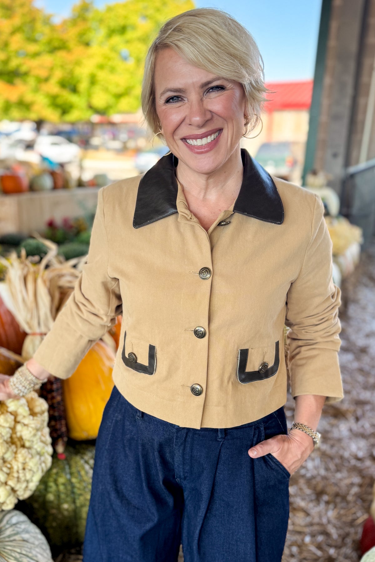 Front view of woman wearing Swagger Boutique’s Taupe Button Up Leather Collared Jacket with jeans standing at a pumpkin patch.