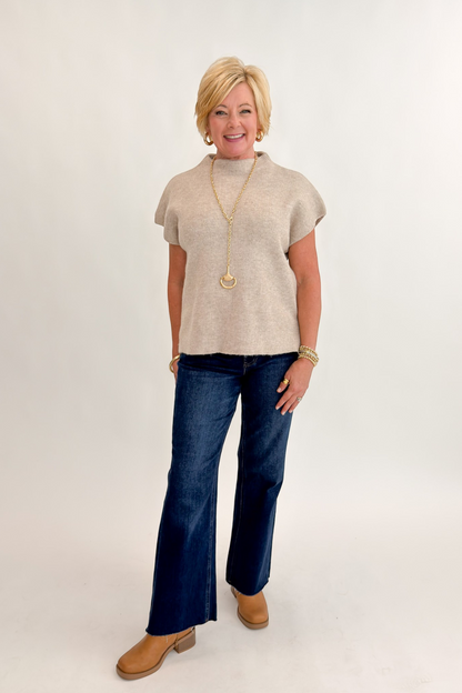 Front view of woman wearing Swagger Boutique’s Taupe Mock Neck Short Sleeve Sweater with jeans against white studio background.