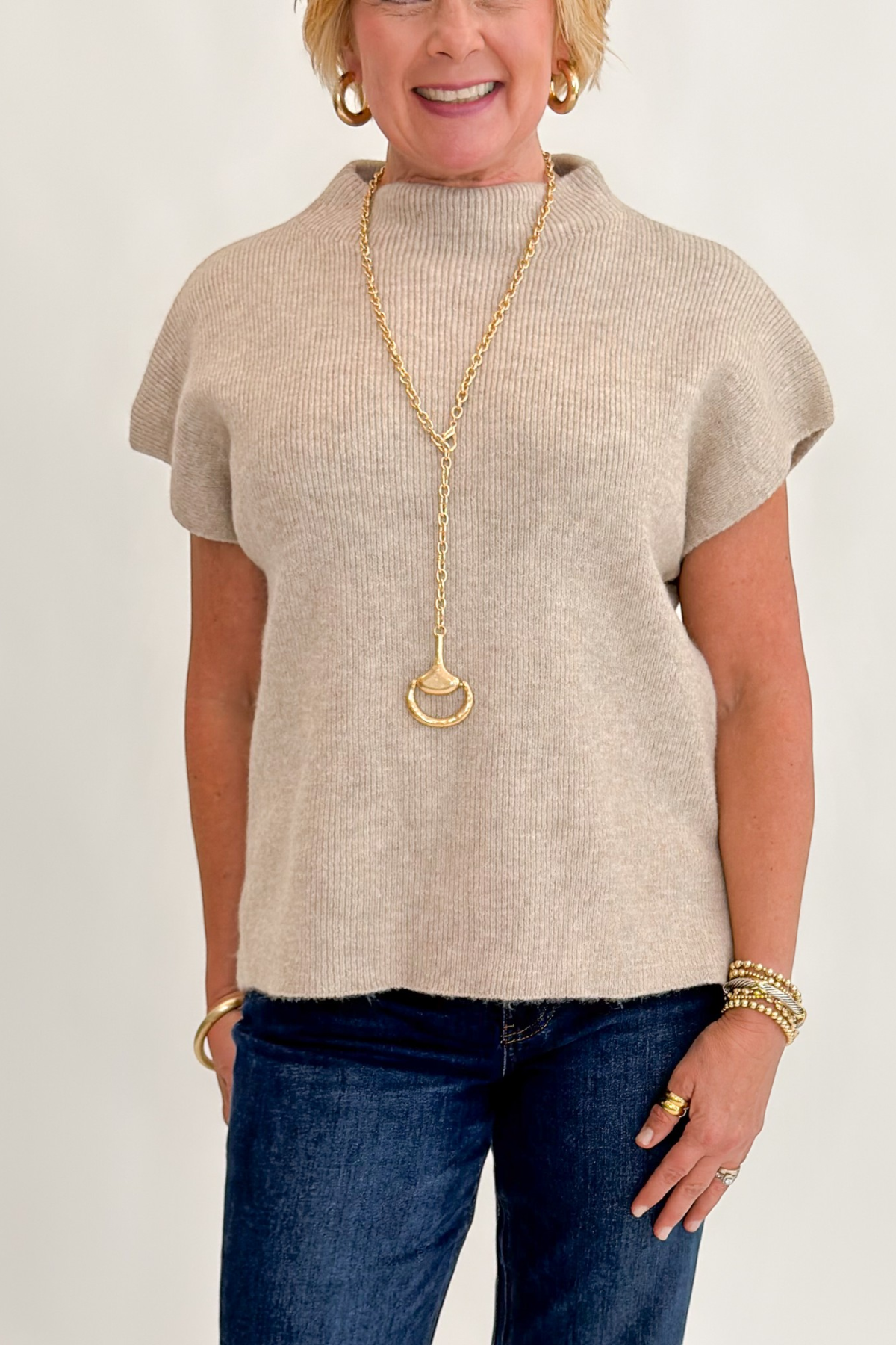 Front detail view of woman wearing Swagger Boutique’s Taupe Mock Neck Short Sleeve Sweater with jeans against white studio background.