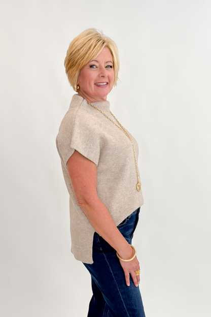 Side view of woman wearing Swagger Boutique’s Taupe Mock Neck Short Sleeve Sweater with jeans against white studio background.