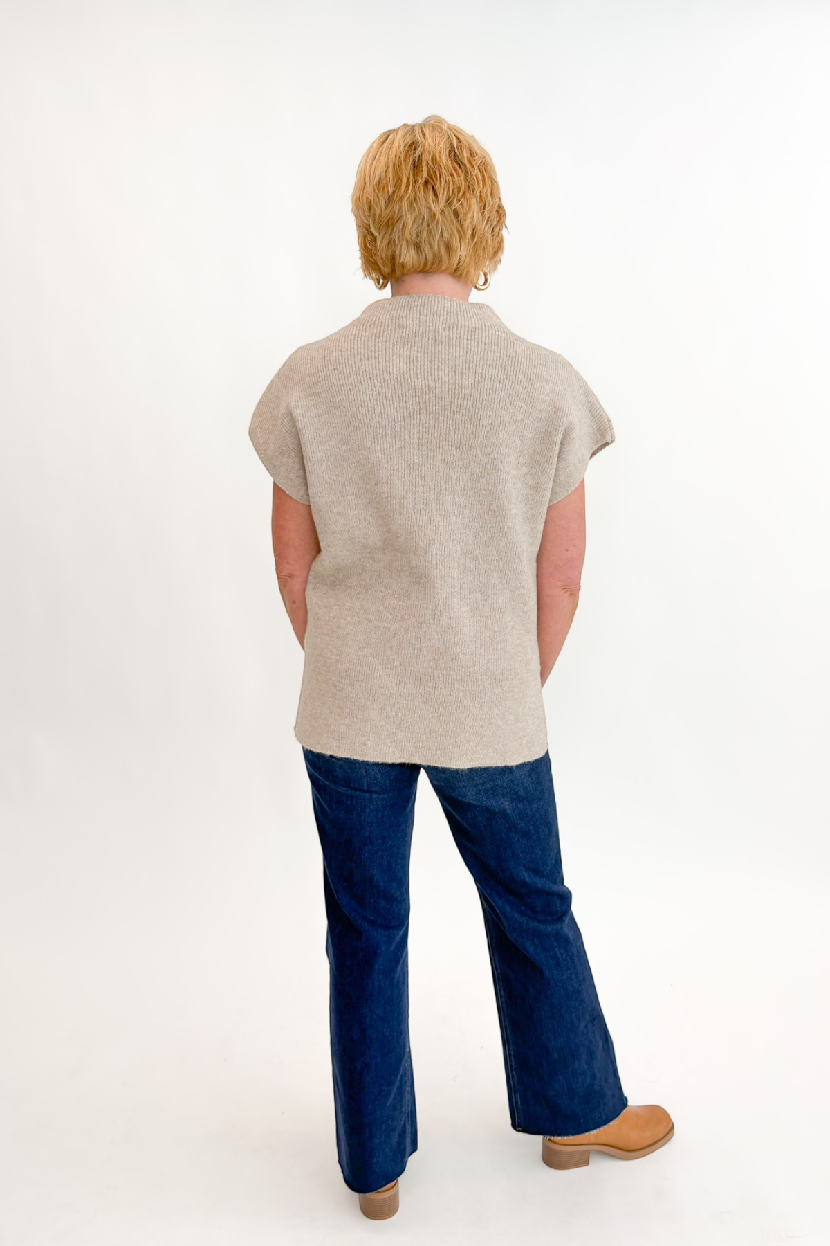 Back view of woman wearing Swagger Boutique’s Taupe Mock Neck Short Sleeve Sweater with jeans against white studio background.
